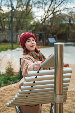 Young girl is happily playing music on outdoor tubular bells in an urban parkの写真素材