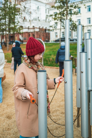 Young girl is happily playing music on outdoor tubular bells in an urban parkの写真素材
