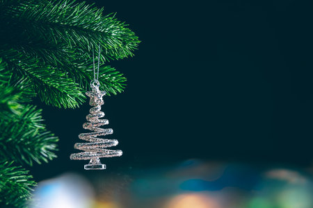 Silver glitter christmas tree ornament hanging on a christmas tree branch with bokeh lights in background with copy spaceの写真素材
