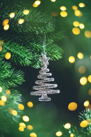 Silver christmas tree ornament hanging on a real christmas tree branch with warm white lights creating a festive bokeh effect in the backgroundの写真素材
