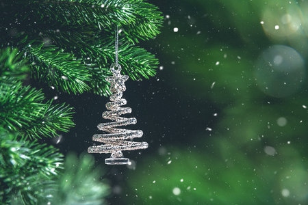 Silver spiral christmas tree ornament hanging from a green branch on dark background, creating a festive and magical atmosphere with copy spaceの写真素材