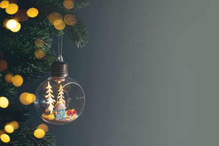 Glass light bulb ornament containing miniature snowy house and trees hanging on christmas tree branch against dark background. Copy space, greeting cardの写真素材