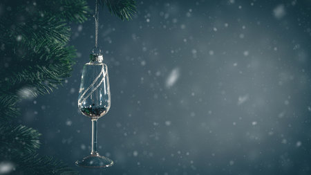 Glass christmas ornament shaped like a champagne glass hanging from a christmas tree branch, with a dark background and copy spaceの写真素材