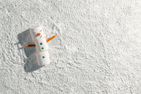 Funny marshmallow snowman lying on snow, creating a snow angel with pretzel stick arms, capturing the playful spirit of winter holidays and festive celebrationsの写真素材