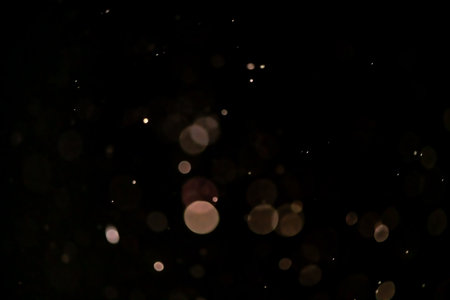Swirling golden particles against a black background, creating a magical and sparkling bokeh effect. Ideal for enhancing festive and celebratory designs with elegance and glamorの写真素材