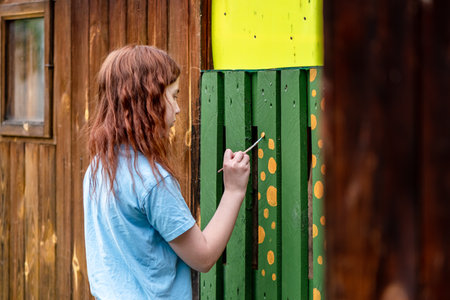 Teenage girl paints a building outdoors in the country, with her own handsの写真素材