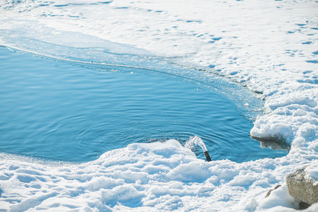 Water gushing from a pipe into a vibrant blue polynya amidst a snow-covered, icy landscape, creating...
