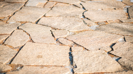 Sunlight illuminates an irregular stone paving, creating a rustic and textured pathway with varying shapes and sizes of stones, adding character to an outdoor spaceの写真素材