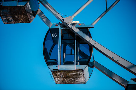 Ferris wheel cabin number six hanging against a vibrant blue sky, creating a striking contrast between the metal structure and the clear skyの写真素材