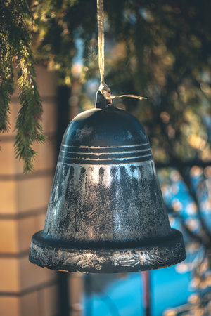Old metallic bell with worn paint and gold ribbon hangs from a tree branch, evoking the spirit of Christmas with its rustic charm and festive presenceの写真素材