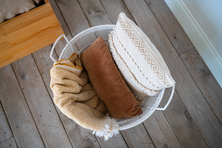 Cozy home decor featuring a white wicker basket filled with a yellow patterned blanket and beige and...