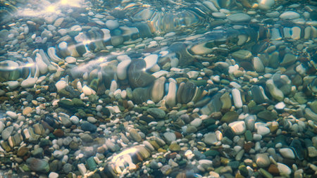 multi-colored stones under water on the sea, river. Natural background of stones, glare on the waterの写真素材