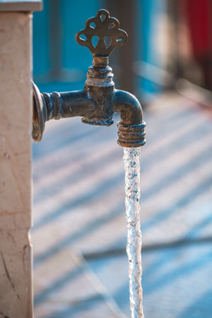 Water flows from an ornate outdoor faucet mounted on a stone pillar, cascading down stone steps in a...