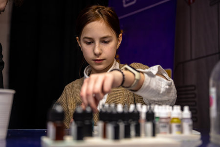 Attentive cute teen girl creating slime during master class, surrounded by ingredients and tools,...