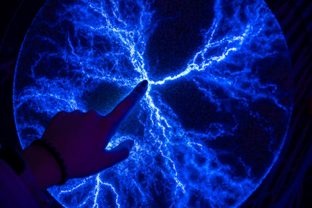 Hand touching a plasma display, creating mesmerizing blue electrical discharges in a dark environment, showing the fascinating interaction between electricity and human touchの写真素材