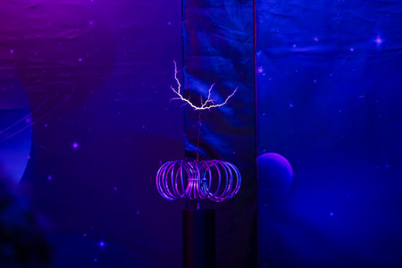 Purple electric sparks emanate from tesla coil in a dark room with starry background, showing...