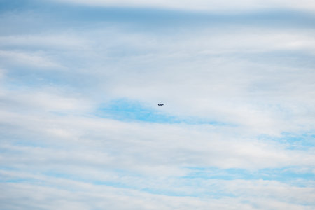 Small airplane soaring high in a partly cloudy sky, leaving a white contrail behind on a stunning...