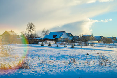 Snow covers the ground around traditional wooden houses with blue painted window frames and wooden fences in a serene winter landscape, showcasing the rustic charm of rural lifeの写真素材