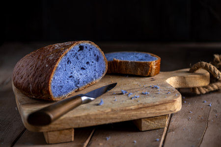 Freshly baked purple bread made with Thai blue ancha tea, partially sliced and resting on a rustic wooden cutting board, looks attractive next to a knife, ready to serve and eat.の写真素材