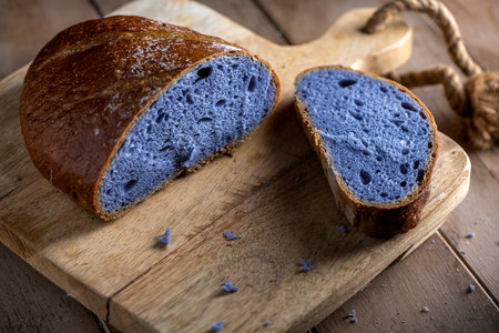 Freshly baked bread with a vibrant purple interior, cooked in blue Thai ancha tea, rests on a rustic wooden cutting board with a slice cut off to reveal its soft, crumbly texture.の写真素材