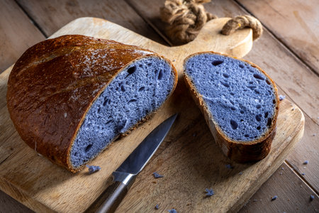 Freshly baked purple bread, partially sliced and resting on a rustic wooden cutting board, looks attractive next to a knife, ready to serve and eat.の写真素材
