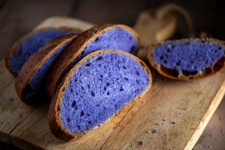 Slices of freshly baked purple bread cooked in blue Thai ancha tea sit on a rustic wooden cutting board, highlighting their vibrant color and unique texture, perfect for food photography.の写真素材
