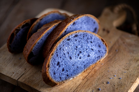 Slices of freshly baked purple bread cooked in blue Thai ancha tea sit on a rustic wooden cutting board, highlighting their vibrant color and unique texture, perfect for food photography.の写真素材