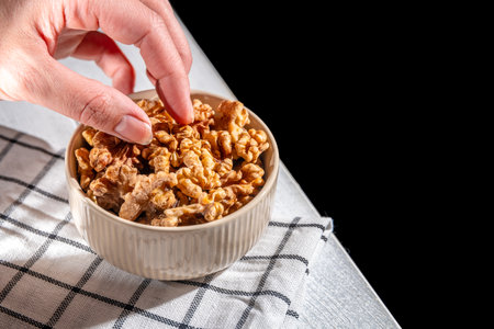 Woman's hand reaches into a bowl of walnuts, picking one from the pile on a checkered cloth, ready...