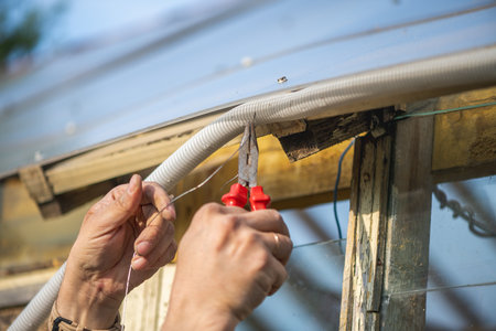 Electrician is working on the electrical wiring of a greenhouse, carefully stripping and connecting...