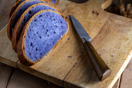 Freshly baked bread with a vibrant purple interior, cooked in blue Thai ancha tea, rests on a rustic...