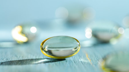 Softgels and fish oil, vitamin D capsules reflecting light against a blue background, creating a...