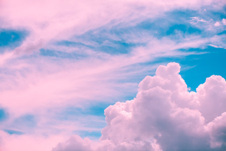 Drifting pink and white cumulus clouds float across a vibrant blue sky, crafting a dreamy and surreal atmosphere that evokes feelings of tranquility and inspirationの写真素材