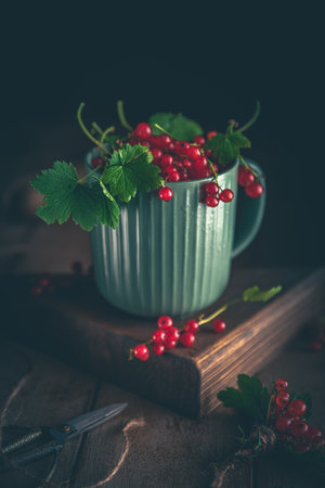 Freshly picked redcurrants spilling from a green mug onto a rustic wooden table, creating a cozy and inviting scene, perfect for food photography or culinary projectsの写真素材