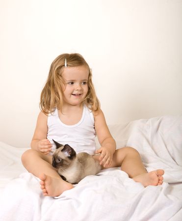 Little girl playing with her kitten in bedの写真素材
