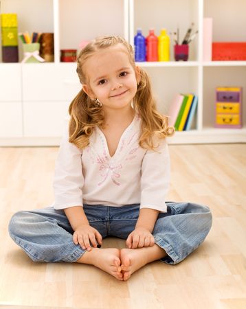 Happy healthy little girl sitting on the floor in her room smiling joyfullyの写真素材