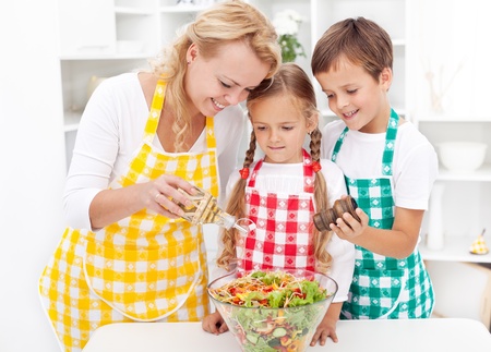 Family in the kitchen seasoning the fresh vegetables saladの写真素材