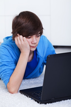 Teenager boy with laptop laying on the floor - computer generation, closeupの写真素材