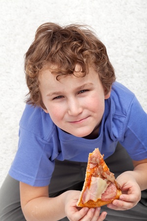 Boy with a slice of pizza sitting on the floorの写真素材