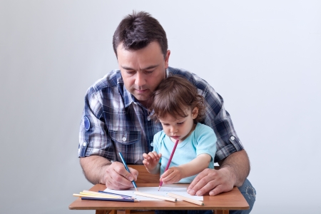 Toddler boy drawing with colored pencils aided by his fatherの写真素材