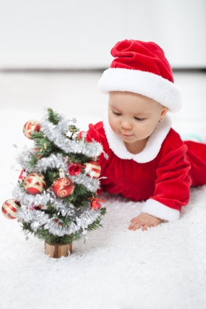 My first christmas - baby girl in santa outfit with small decorated treeの写真素材