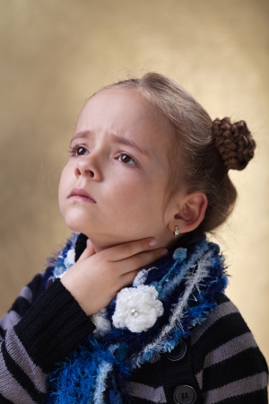 Little girl with sore throat in flu season touching her neckの写真素材