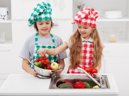 Kids washing vegetables in the kitchen putting them in a strainerの写真素材