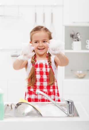Happy little girl washing the dishes having fun with the foamの写真素材