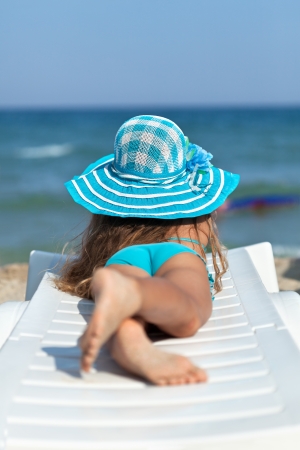 Little girl on the beach relaxing on a deck chair watching the seaの写真素材