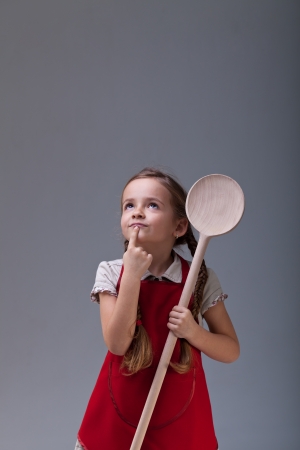Little chef thinking about what to cook - holding a large wooden spoon - with copy spaceの写真素材