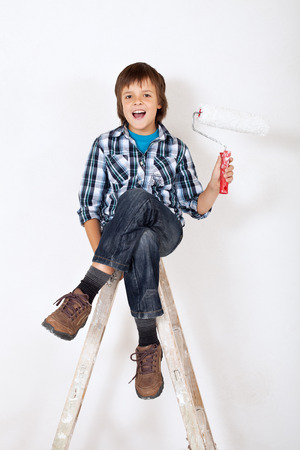 Happy boy with paint roller on top of wooden ladderの写真素材