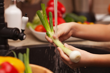 Child hands washing vegetables for a healthy salad in the kitchen sink area - the spring onions, shallow depthの写真素材