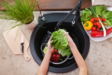 Child hands washing vegetables at the kitchen sink - top view with lettuce leaf under the tapの写真素材