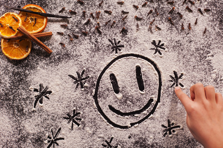 Child hand drawing happy face in the christmas cookies flour spread on table surface, top viewの写真素材