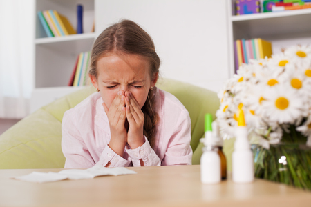 Young girl sneezing at home with paper towel prepared to blow her noise - allergy conceptの写真素材